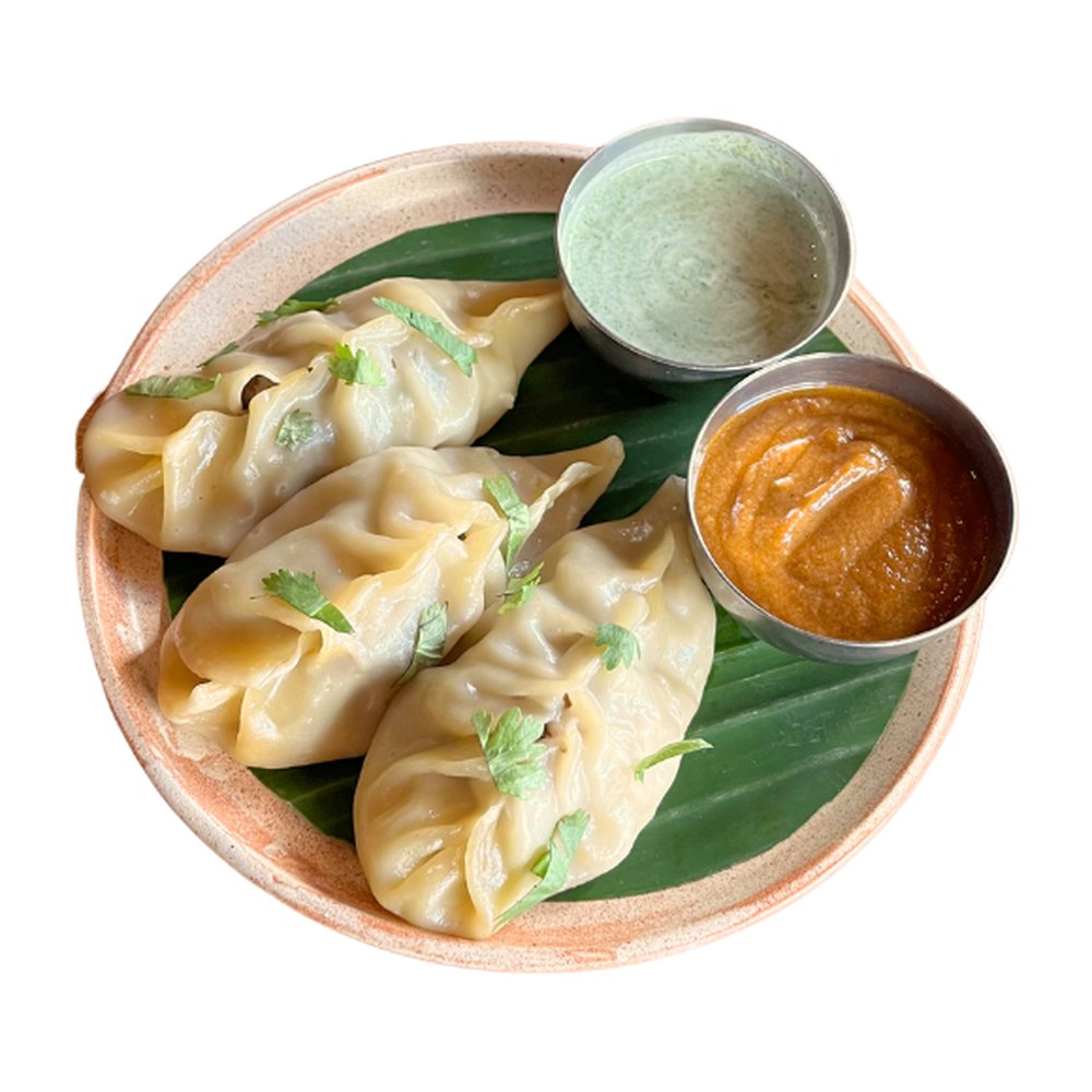 Three steamed chicken momos on a banana leaf with a spicy nutty sauce and a yogurt coriander dip